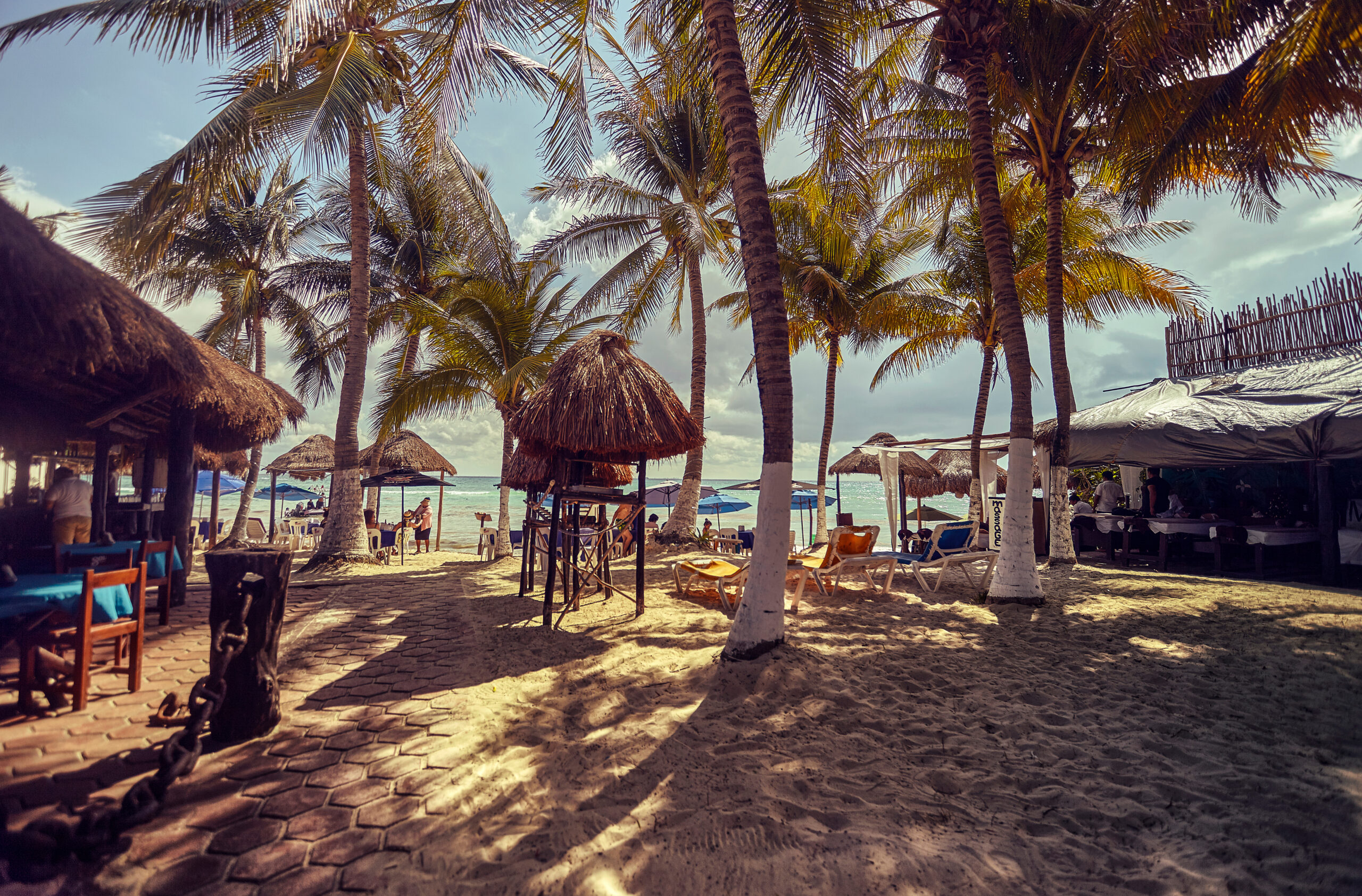 View of a glimpse of Playa del Carmen beach in Mexico, full of palm trees and with some bar huts.